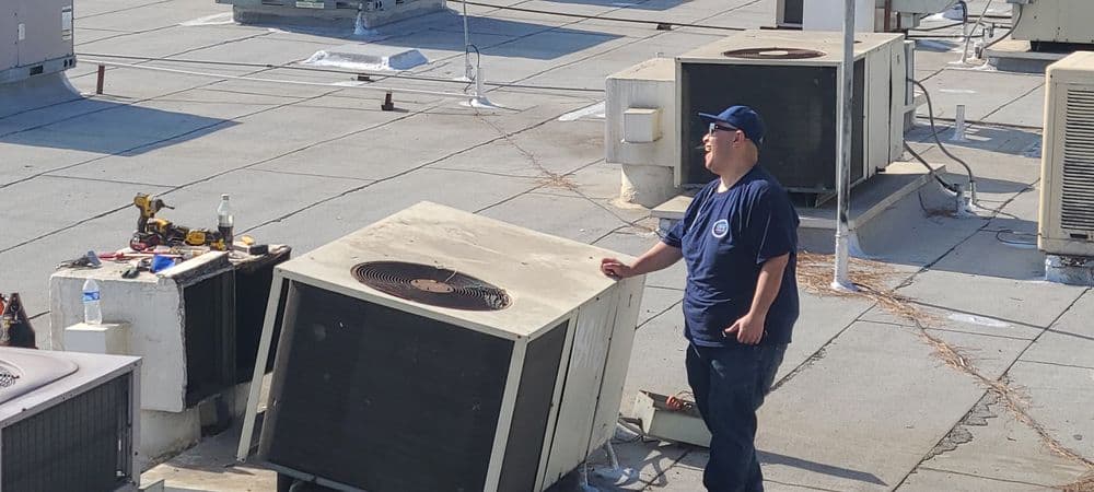 Technician servicing air conditioning units on a commercial rooftop.