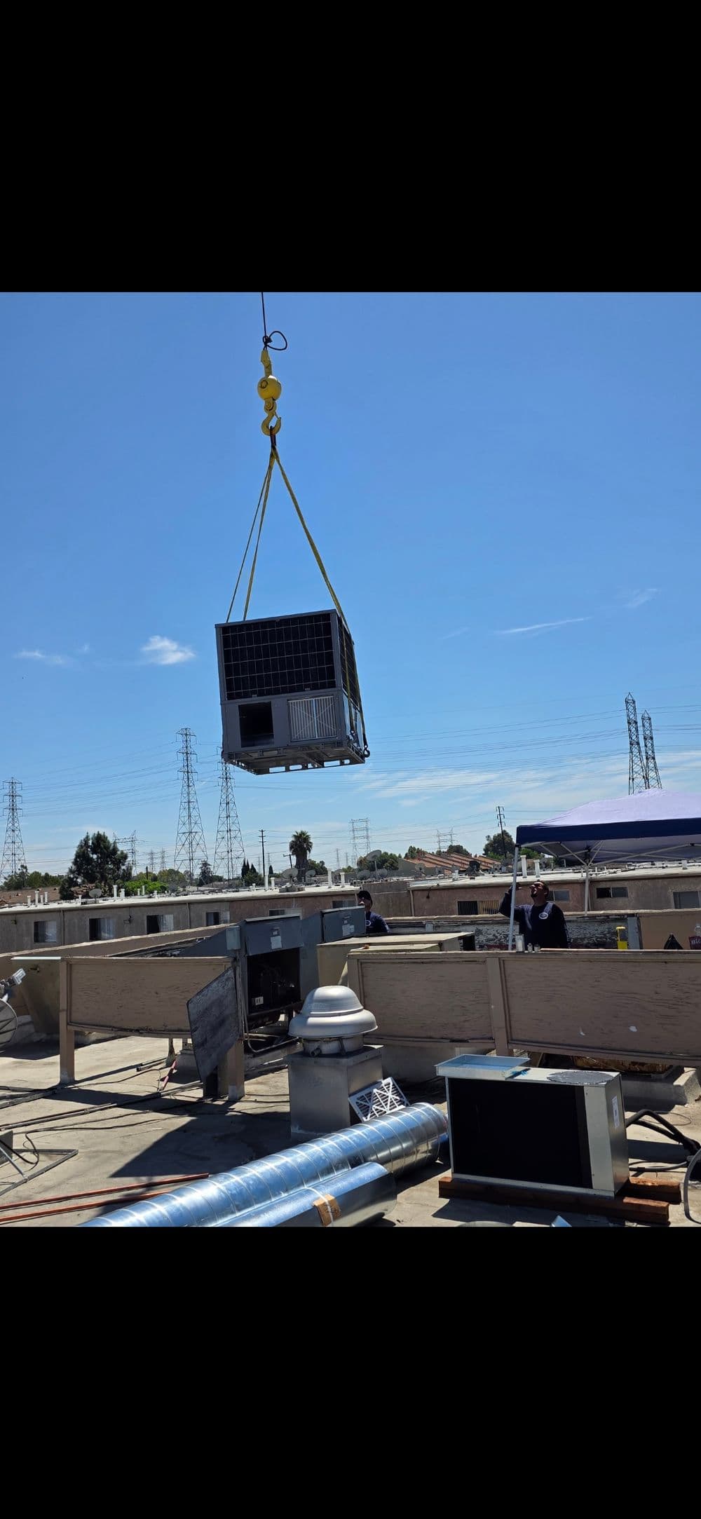 HVAC unit being lifted onto a rooftop for installation on a sunny day.