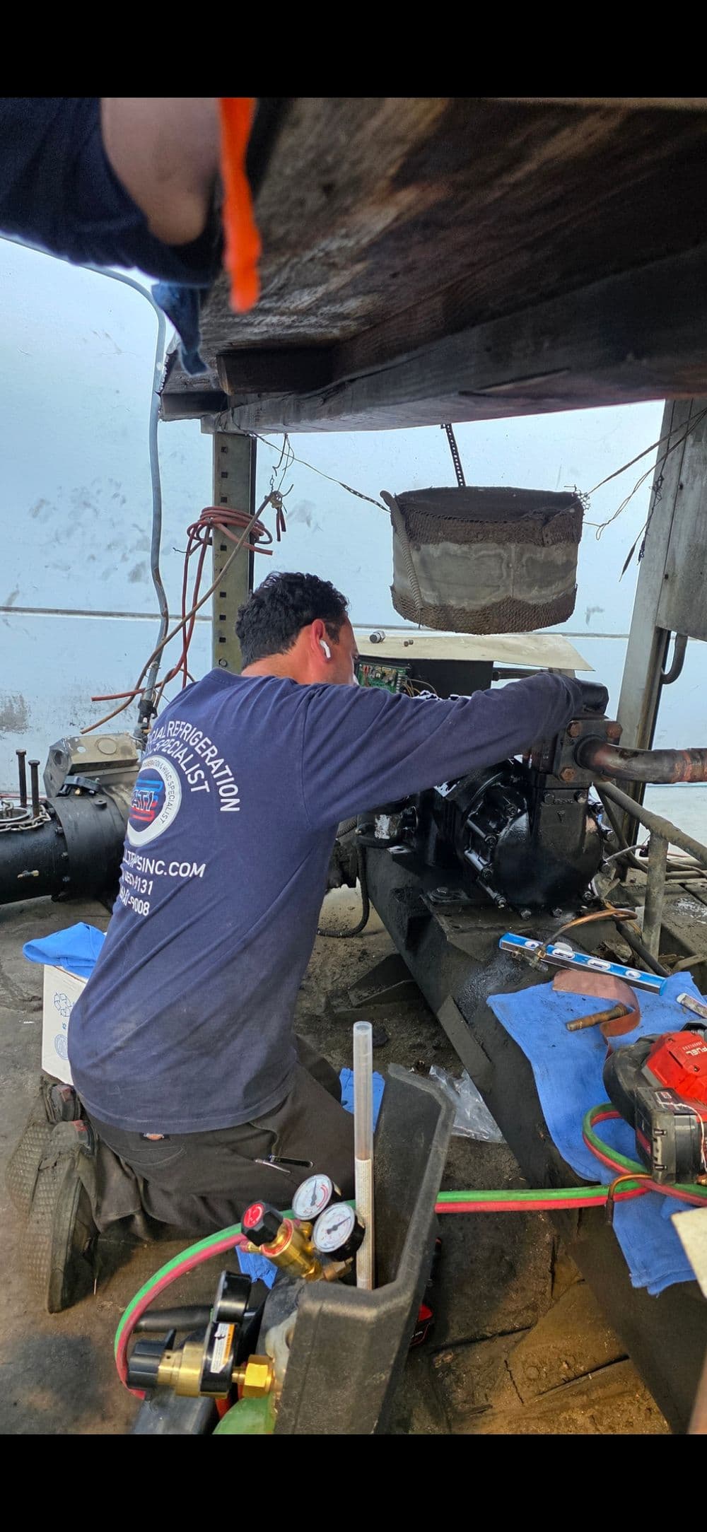 Mechanic working on an engine in a workshop, using tools and wearing ear protection.