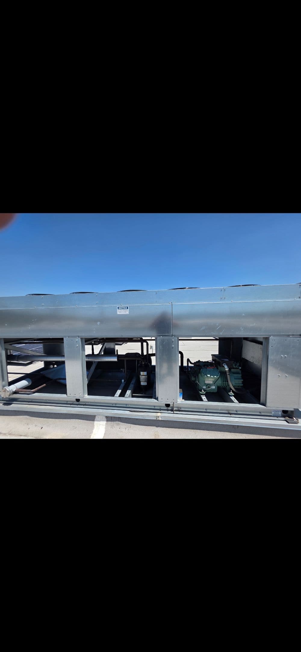 Industrial cooling system with visible compressor and condenser units under clear blue sky.