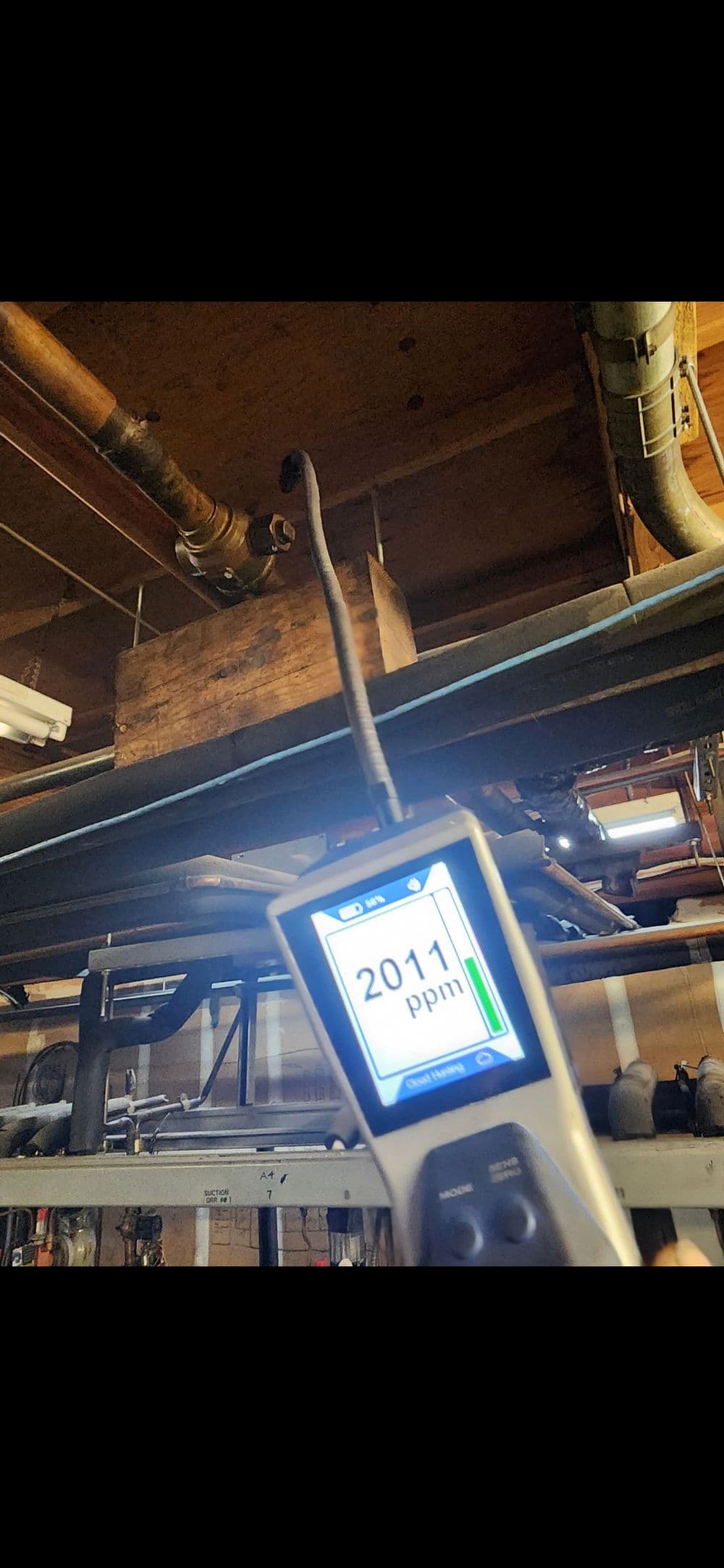 Gas detector reading of 2011 ppm in a building with exposed pipes and wooden box.