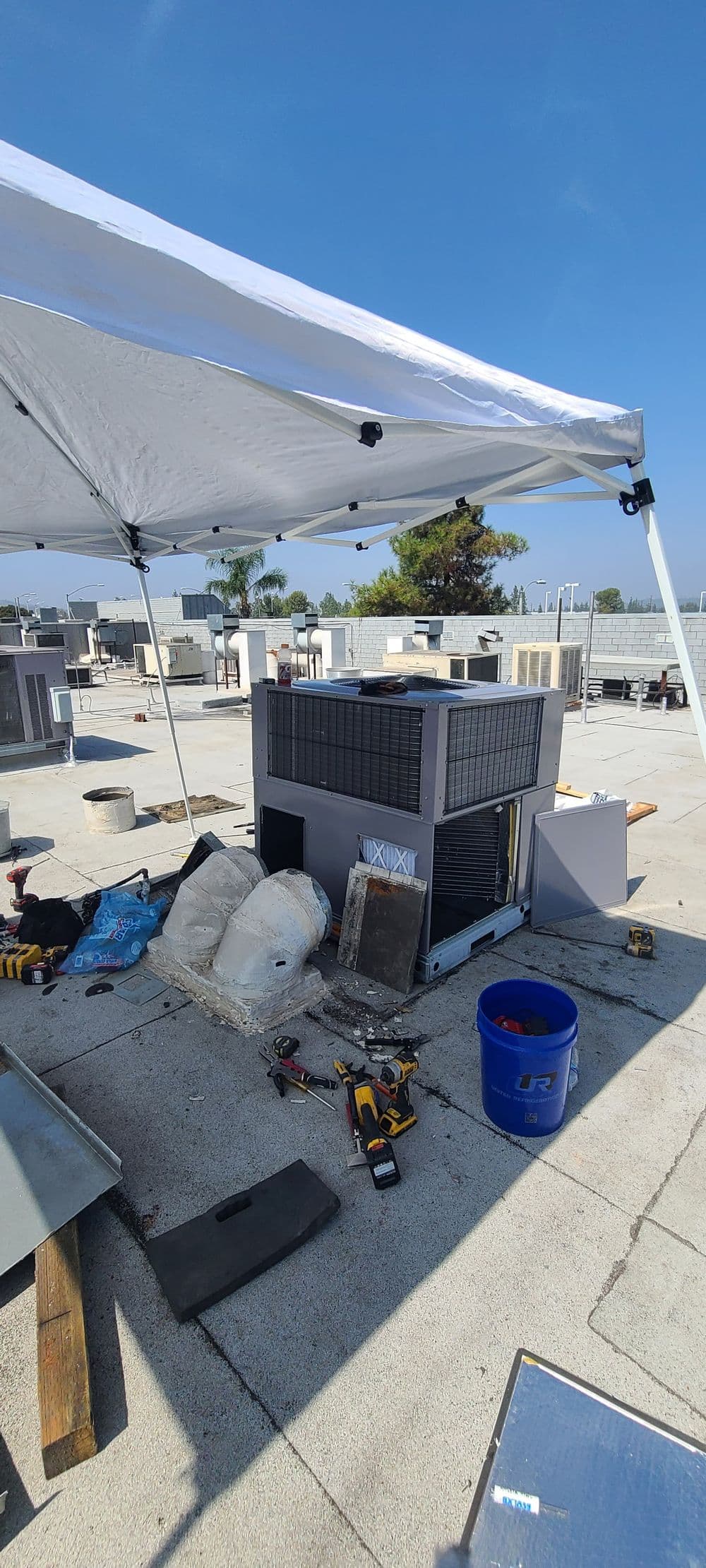 Roofing equipment and tools under a tent on a commercial rooftop installation site.