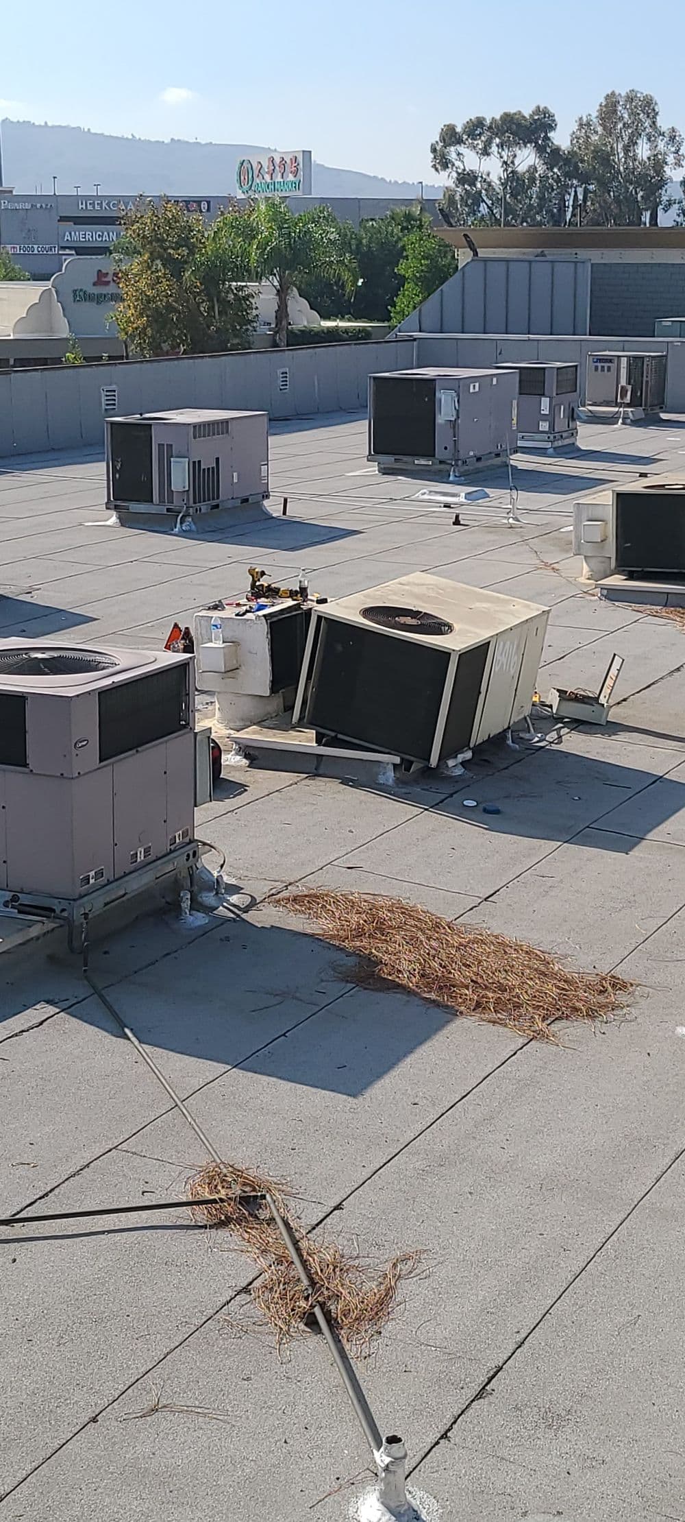 Commercial rooftop air conditioning units, some tilted, with debris and maintenance tools visible.