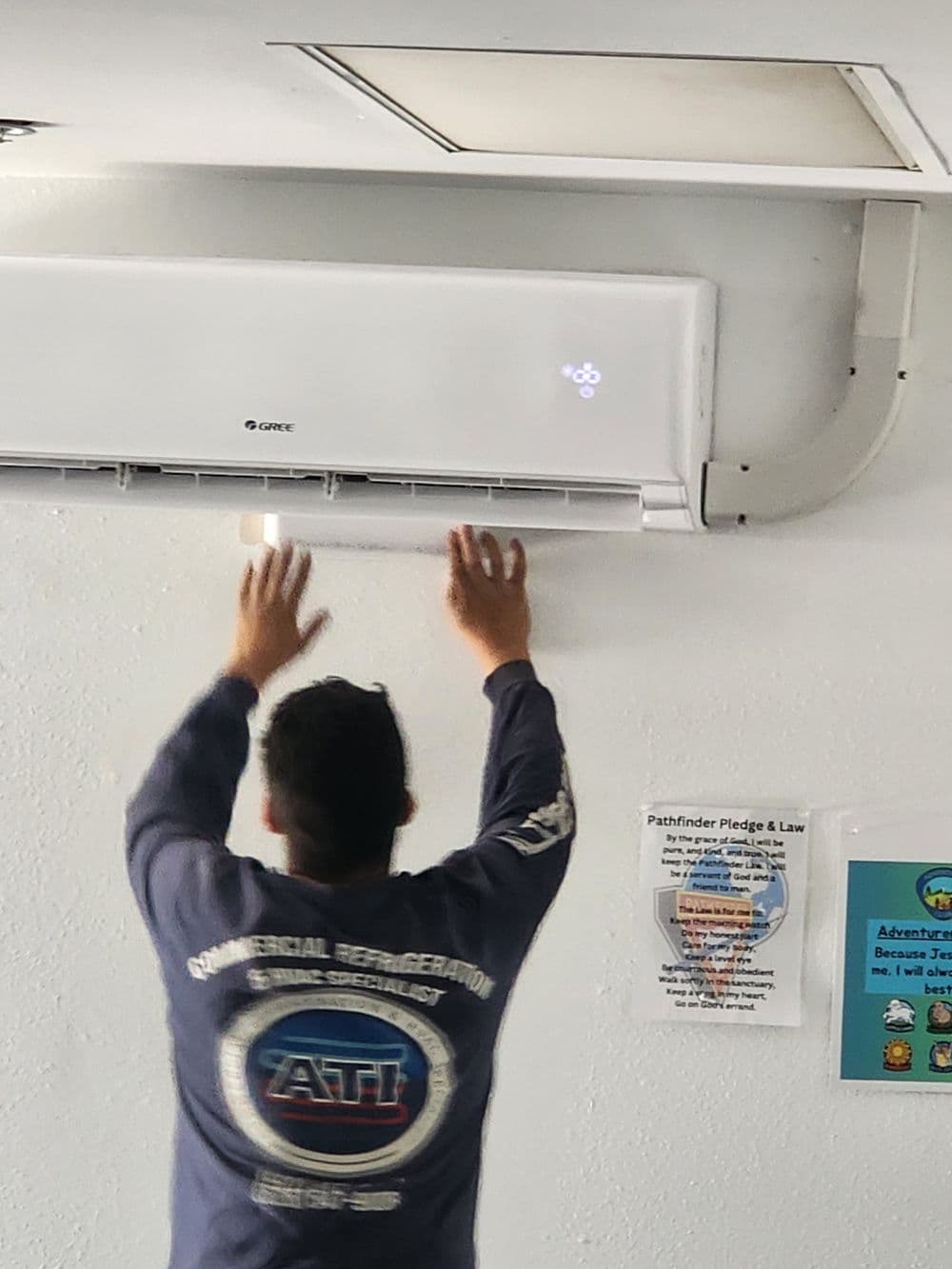Technician adjusting air conditioning unit in a commercial space.