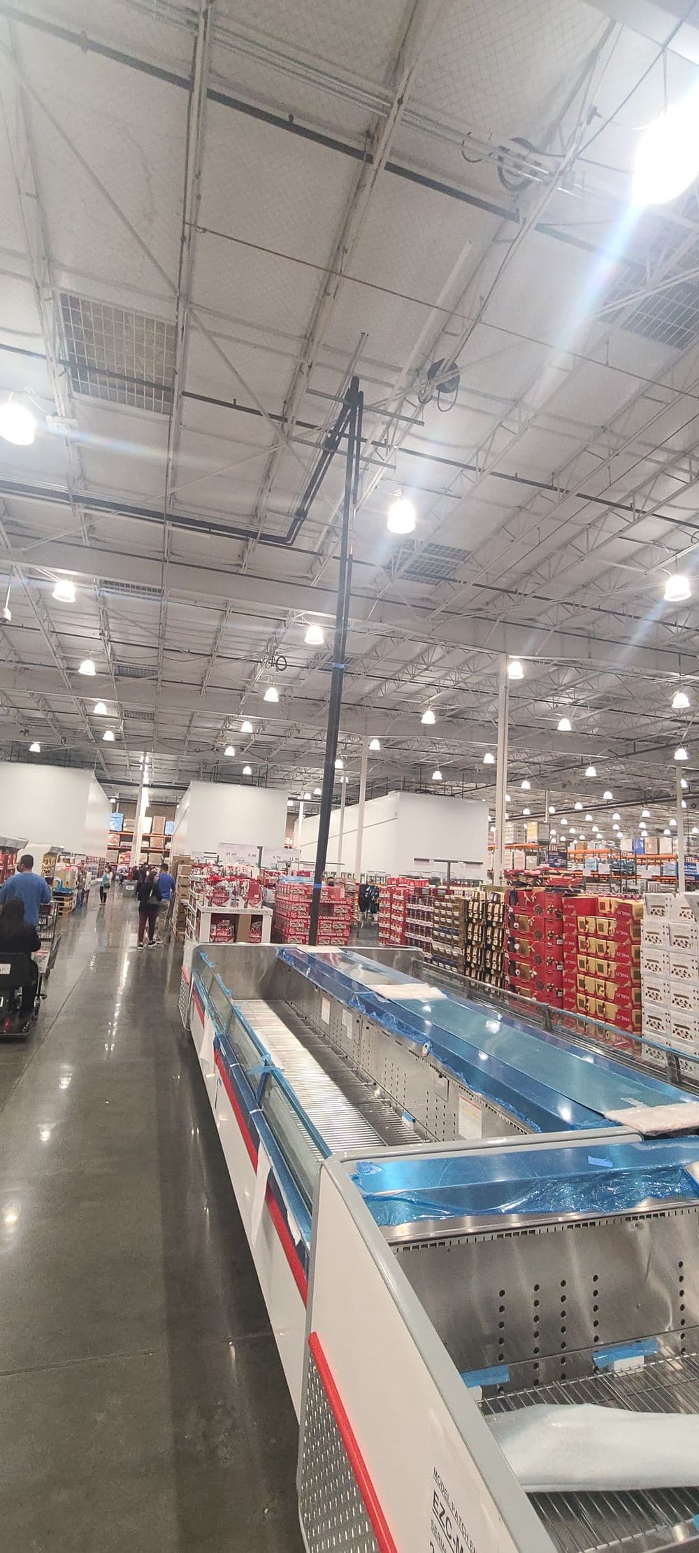 Interior of a Costco store showing aisles, freezer section, and shoppers browsing products.