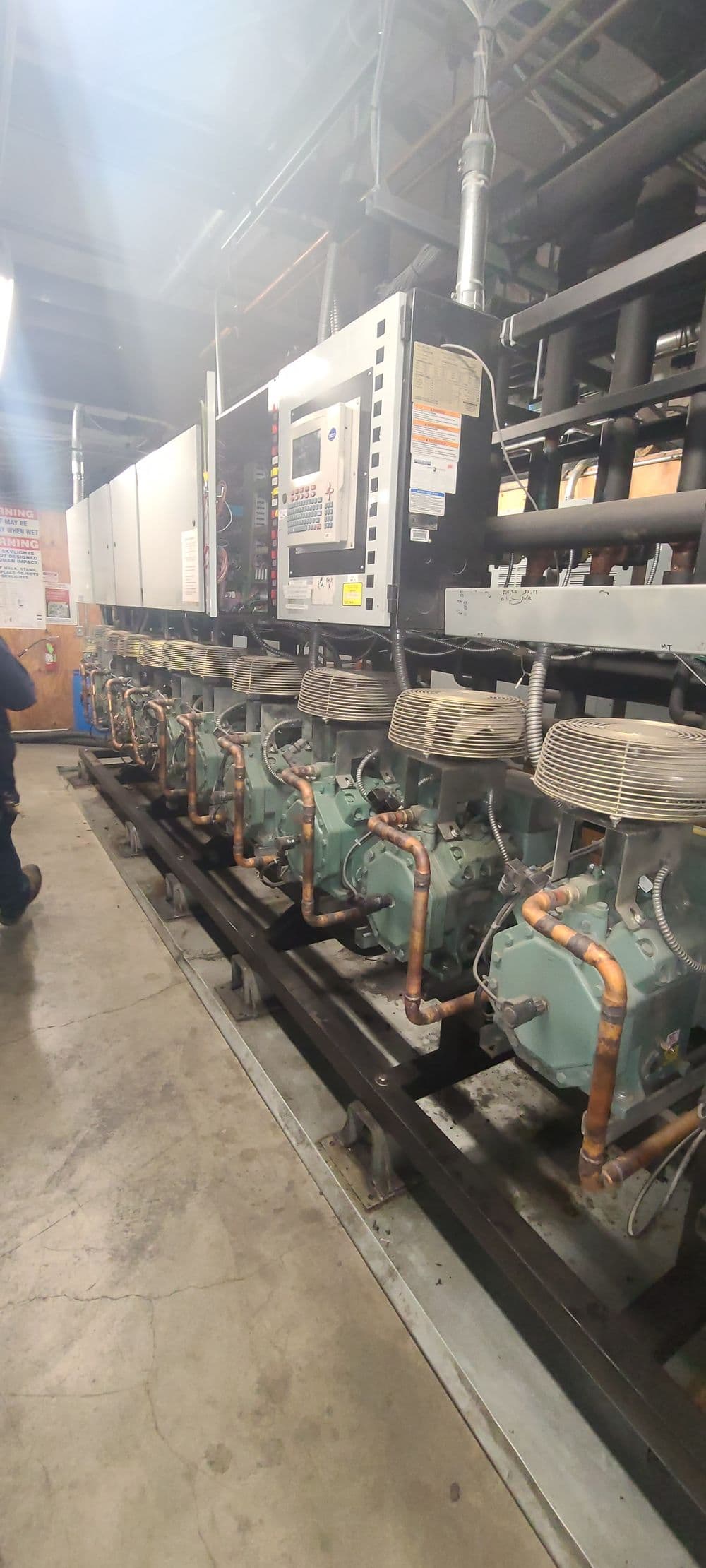 Industrial refrigeration system with multiple compressors and control panel in a mechanical room.