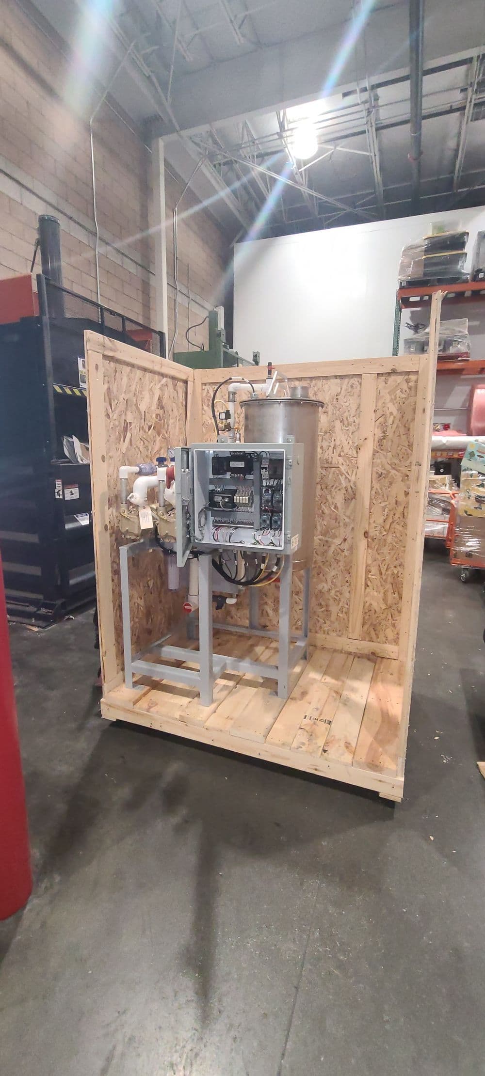 Industrial equipment housed in wooden enclosure, featuring control panel and piping.
