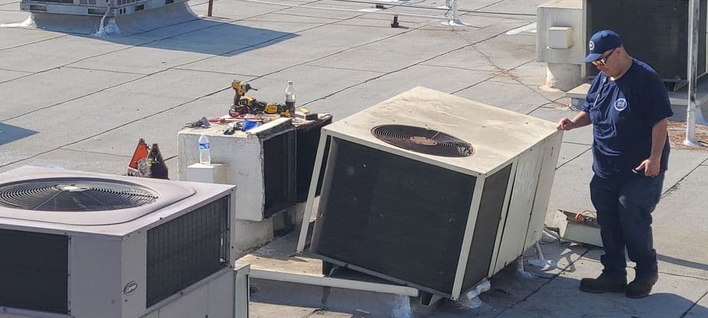 Technician repairing tilted air conditioning unit on rooftop with tools.