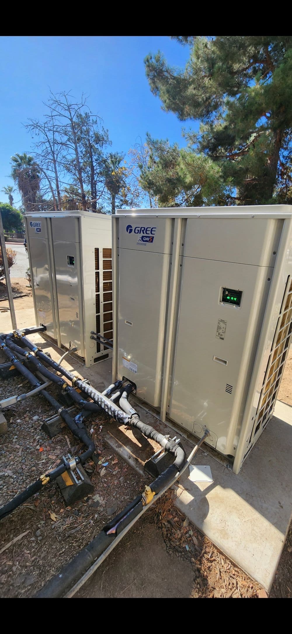 GREE air conditioning units installed outdoors with connecting pipes and clear blue sky.