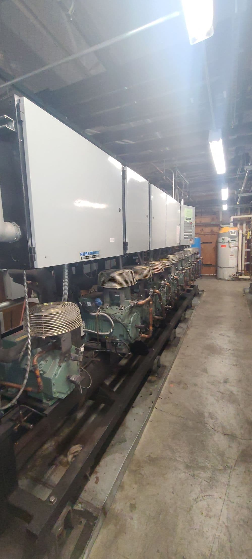 Industrial refrigeration system with multiple compressors and units in a facility hallway.