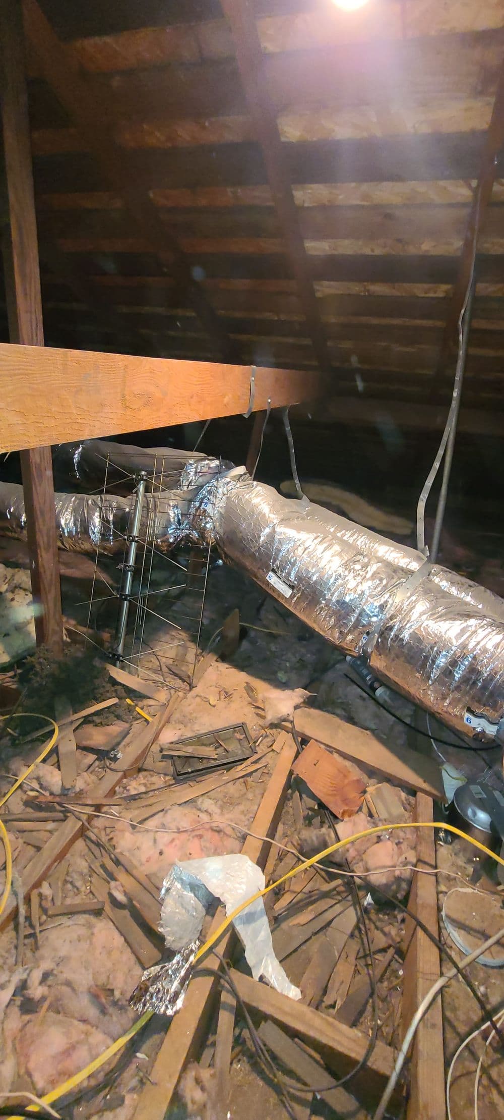 Ductwork in an unfinished attic with insulation, exposed wood beams, and electrical wiring.