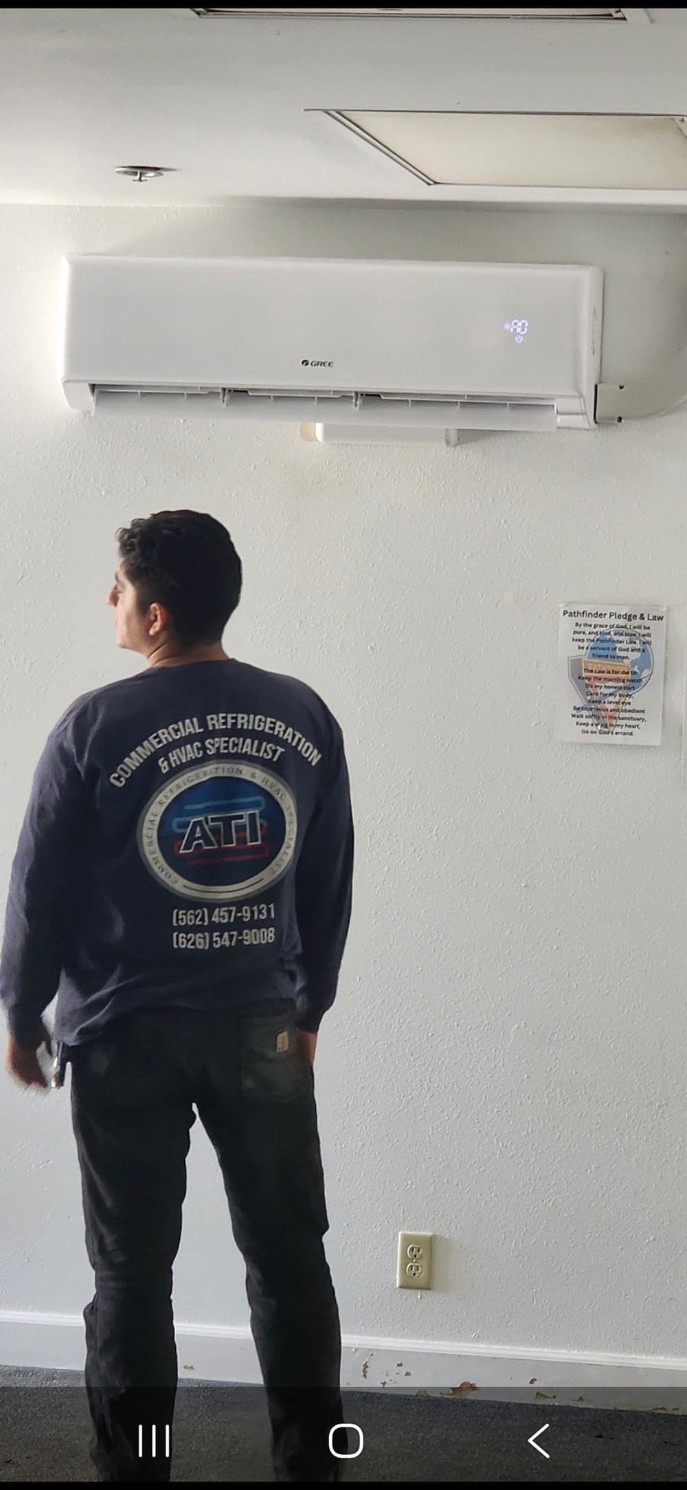 Technician in uniform adjusting wall-mounted air conditioning unit in commercial setting.