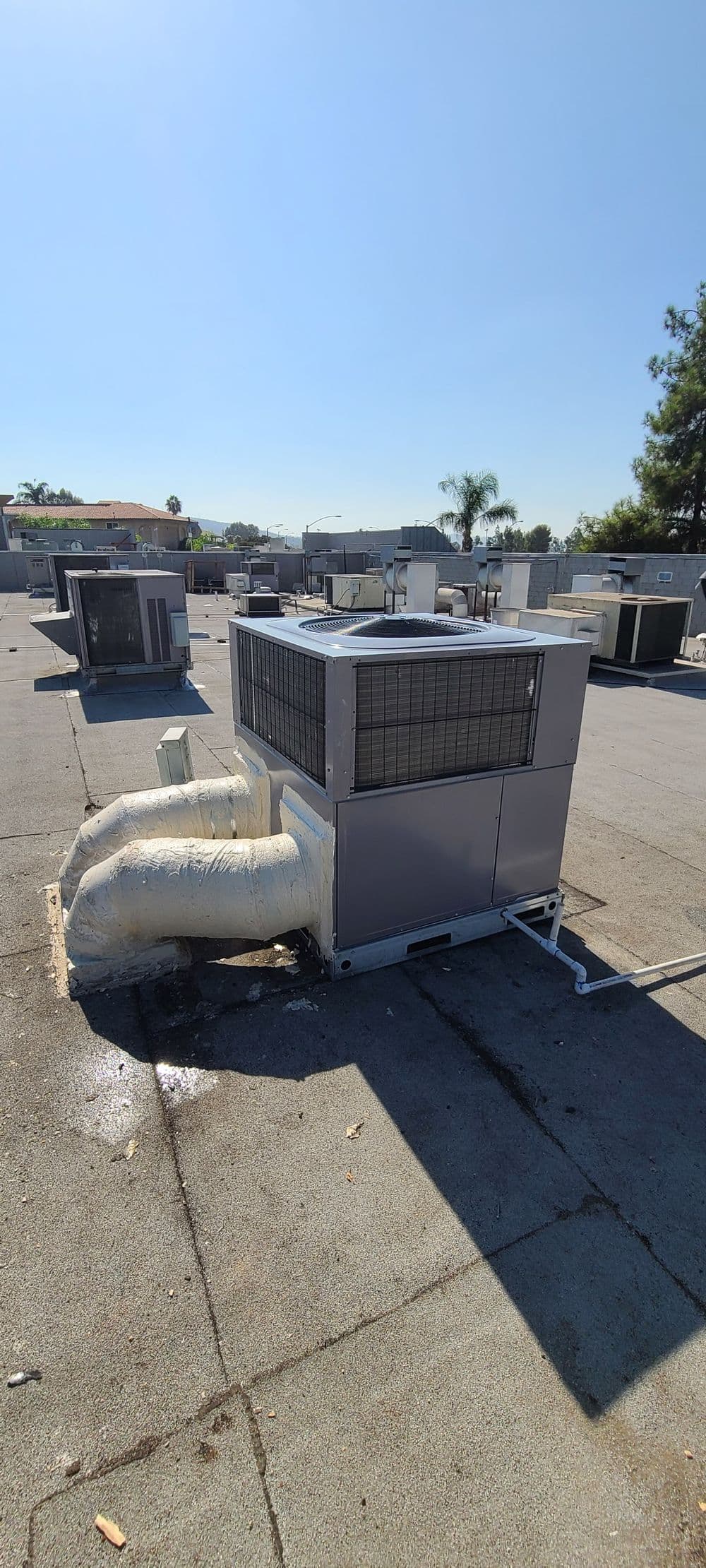 Rooftop air conditioning unit with insulated ductwork against clear blue sky.