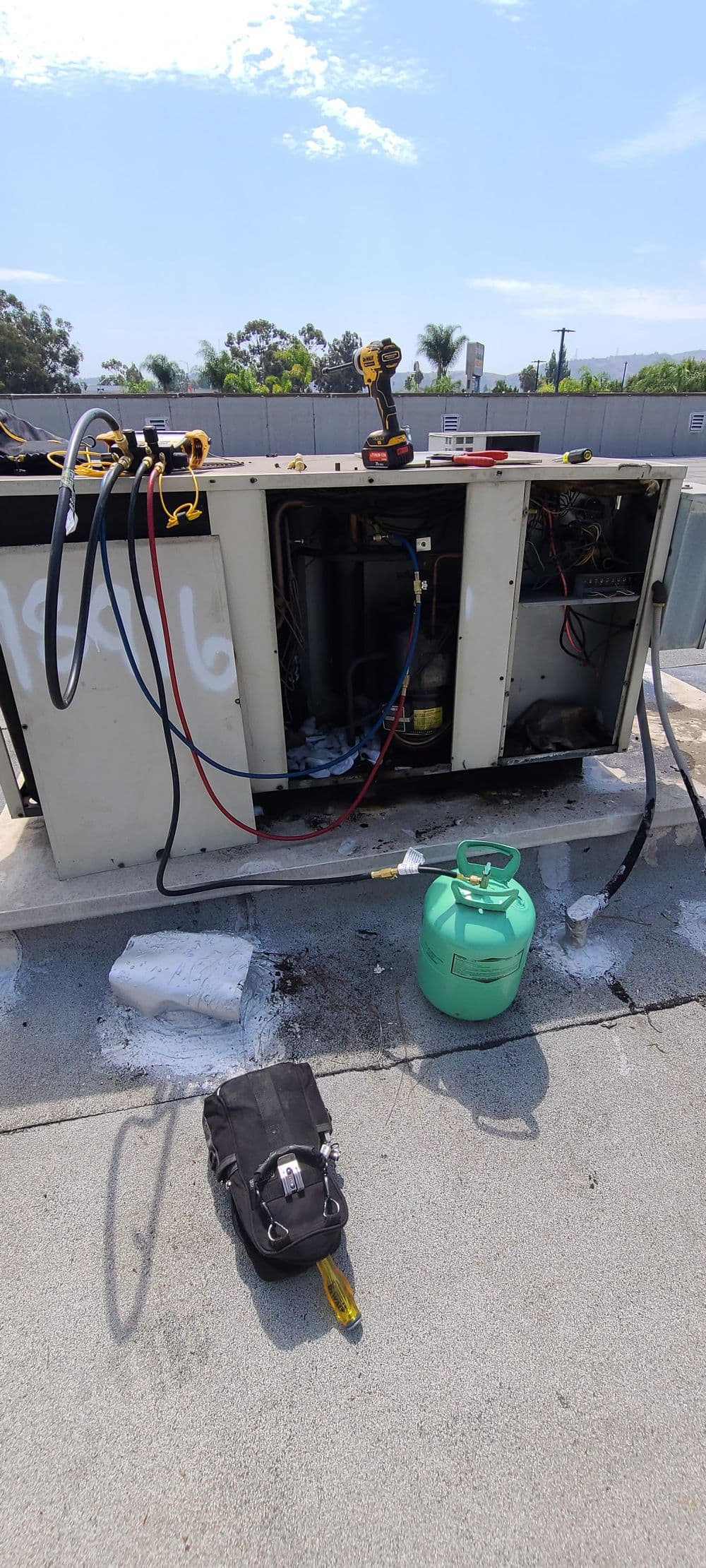 HVAC unit on rooftop with tools, refrigerant tank, and maintenance equipment nearby.