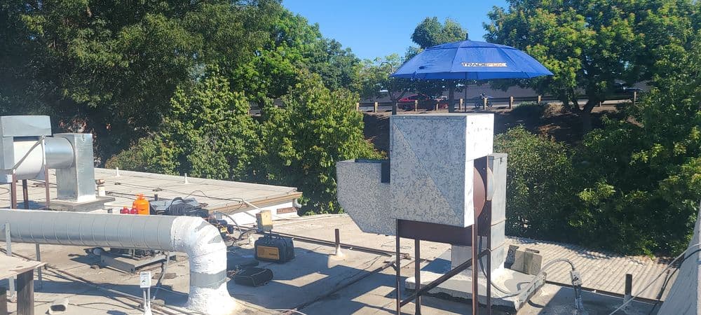 Rooftop with HVAC equipment and blue umbrella providing shade on a sunny day.