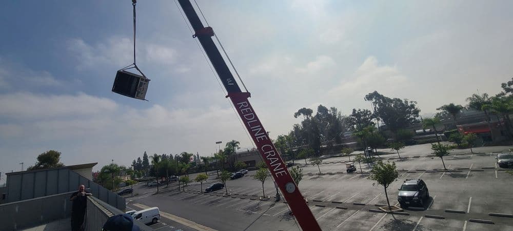 Redline Crane lifting equipment over a parking lot under cloudy sky.