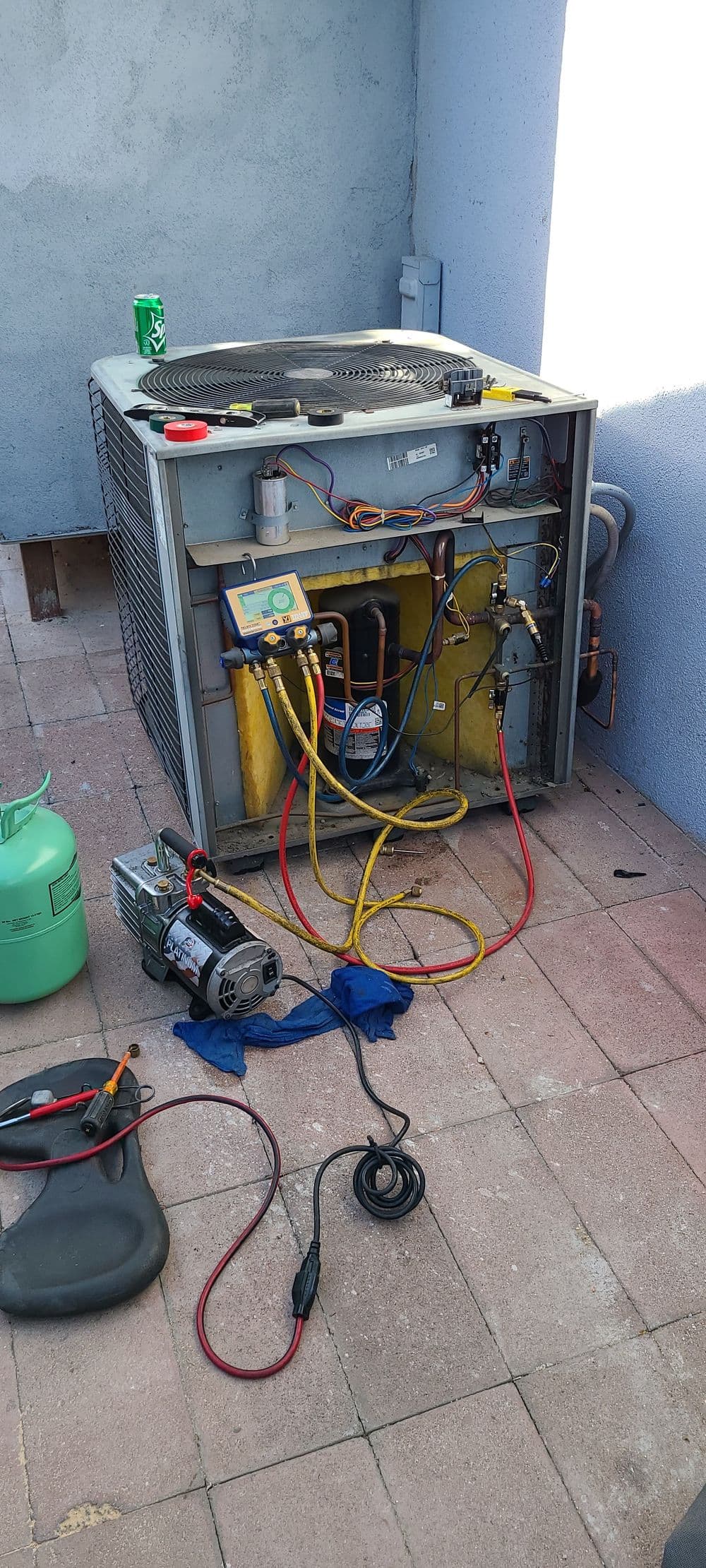 Air conditioning unit being serviced with tools and components on a patio floor.