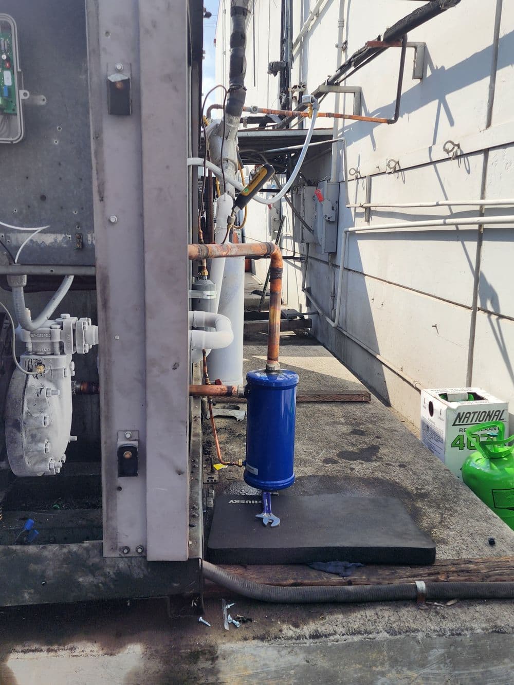 Industrial refrigeration system with blue compressor and copper pipes on exterior platform.