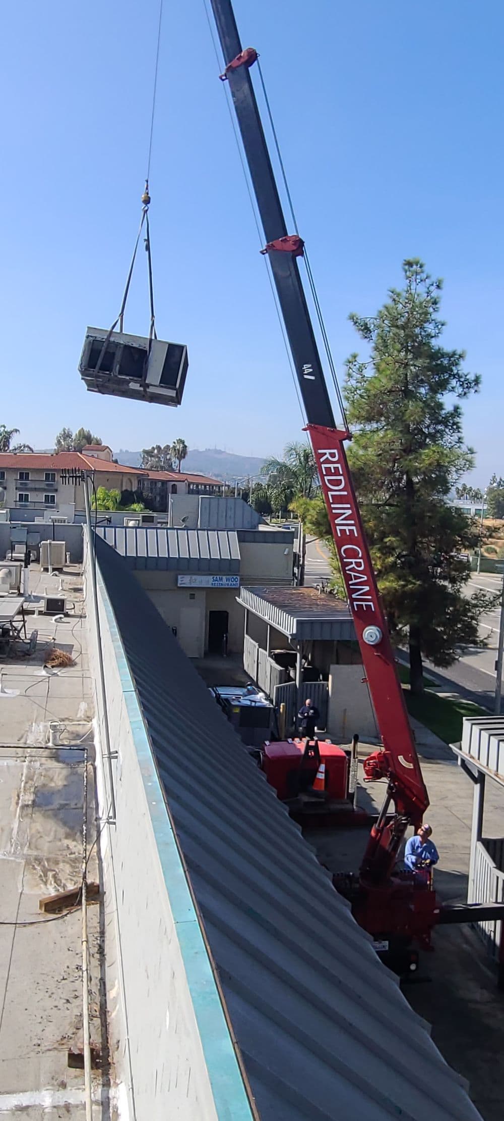 Redline crane lifting equipment over a rooftop at a construction site under blue sky.