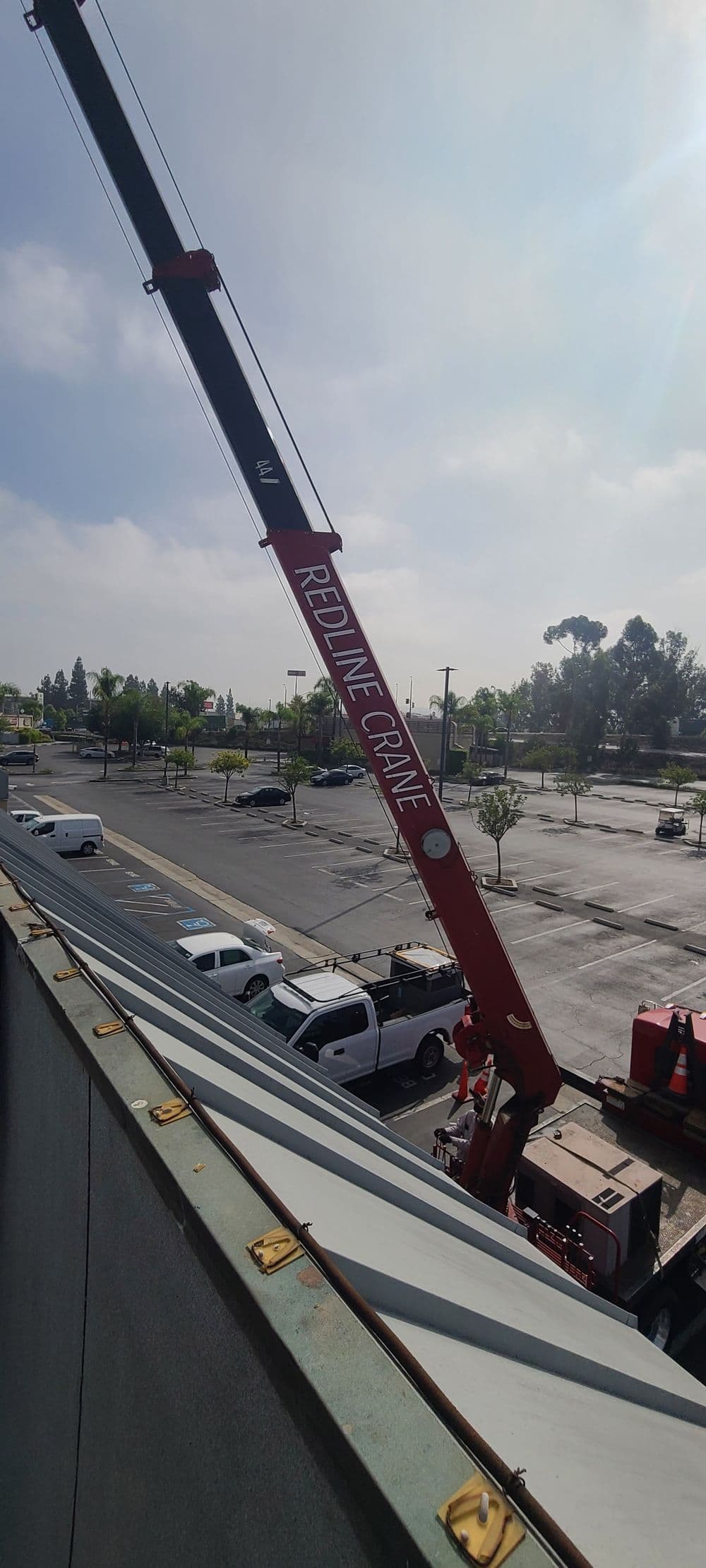 Redline Crane lifting equipment at a construction site with parked vehicles in the background.