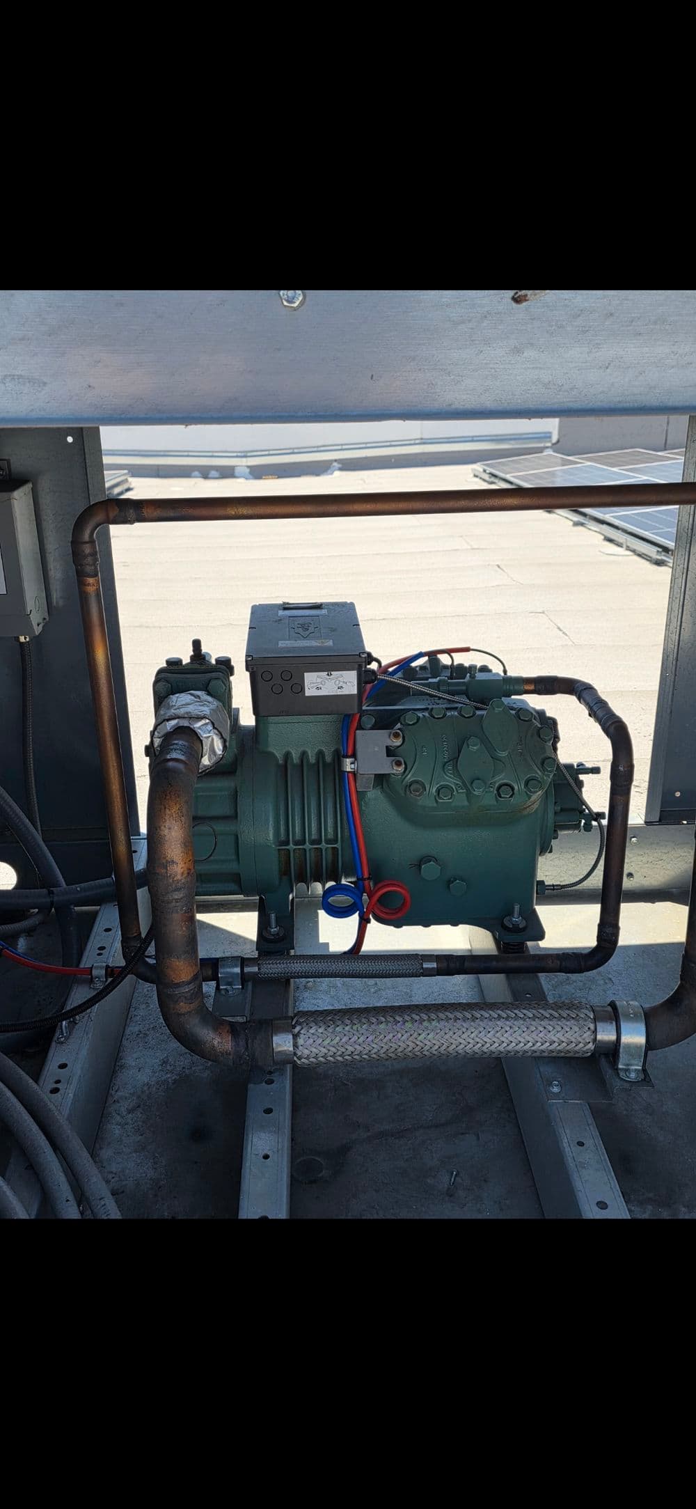 Industrial compressor unit with copper piping and electrical components in outdoor setting.