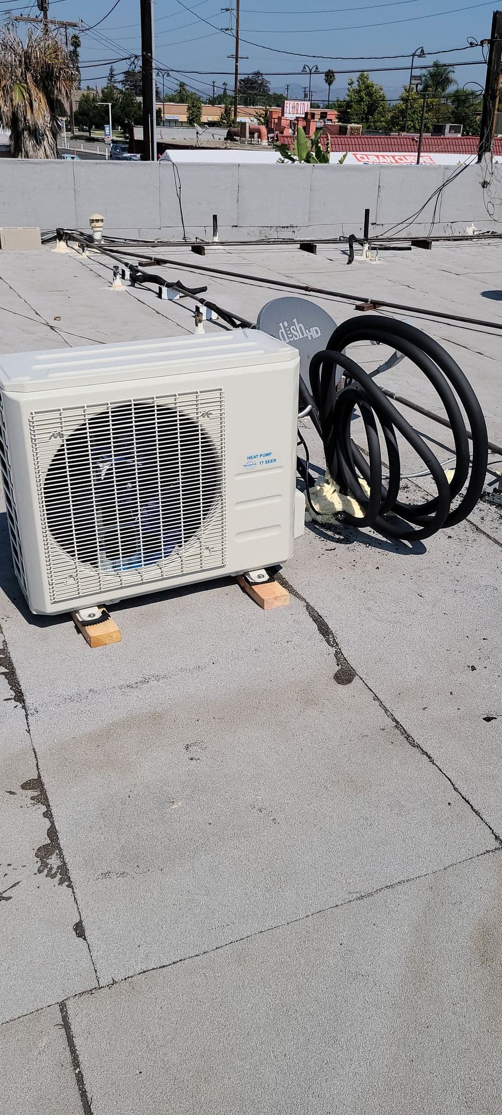 Air conditioning unit on a flat roof with refrigeration lines and electrical connections.