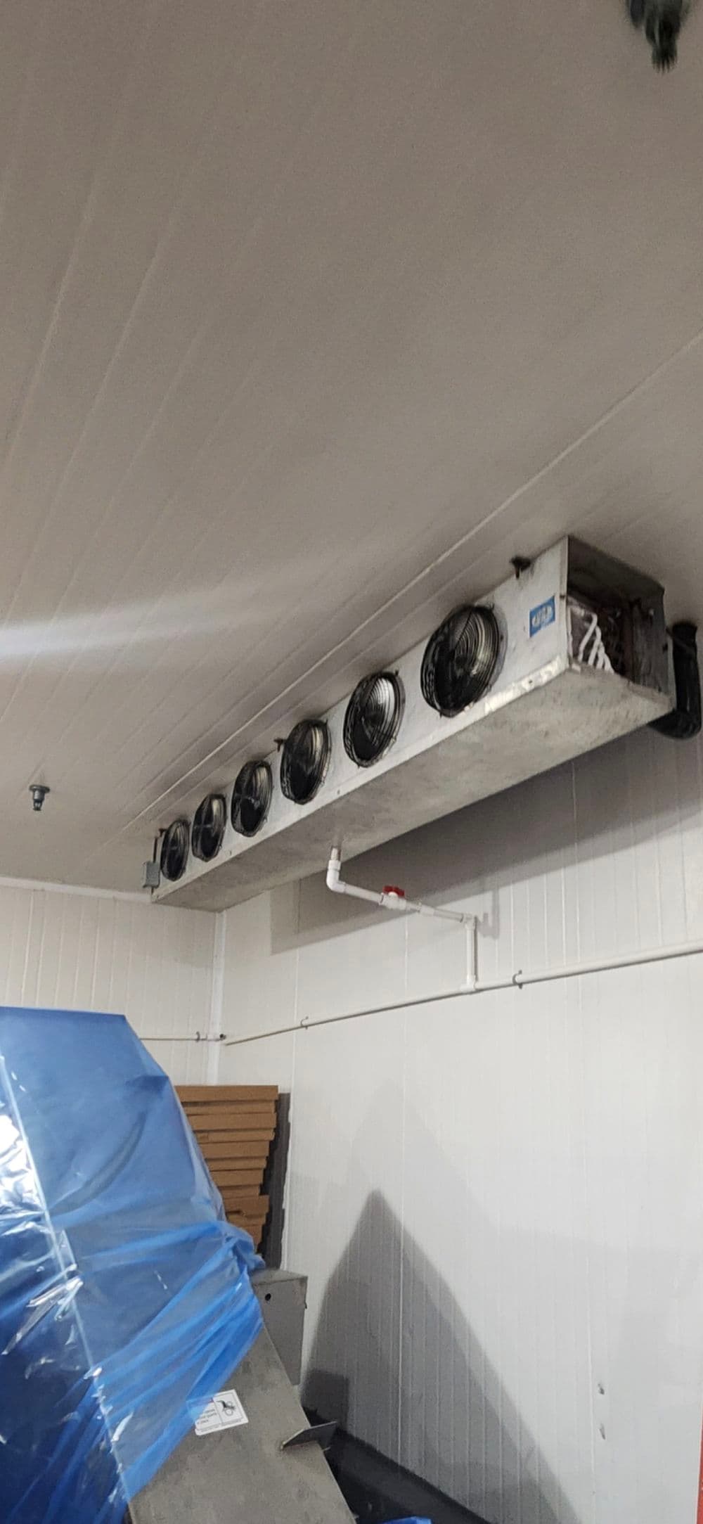Ceiling-mounted refrigeration unit with multiple fans in a commercial storage space.