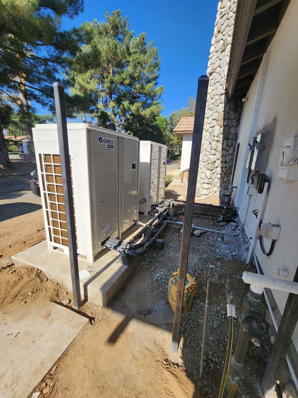 HVAC units installed next to a building with surrounding trees and utility connections.