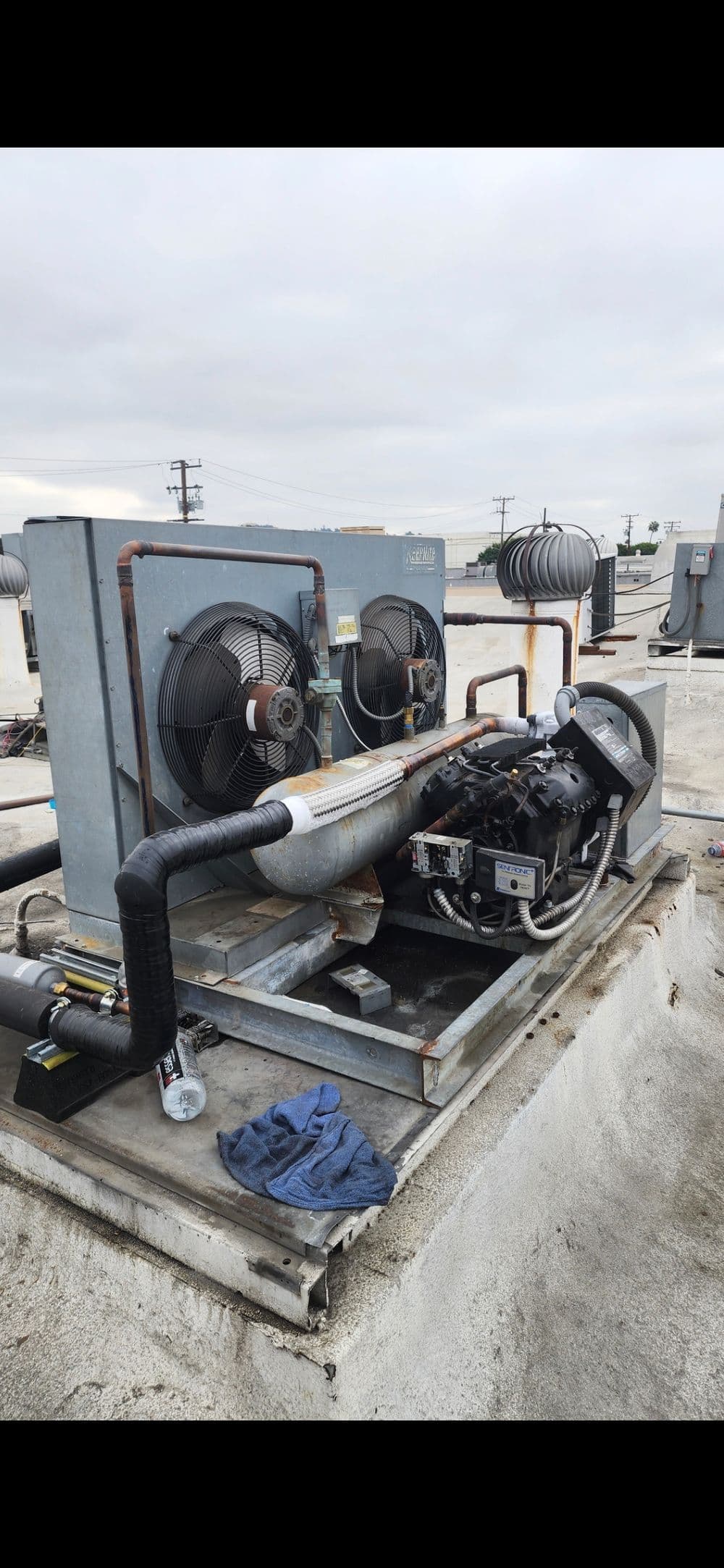 Industrial rooftop cooling unit with fans and compressor, on a cloudy day, for HVAC systems.