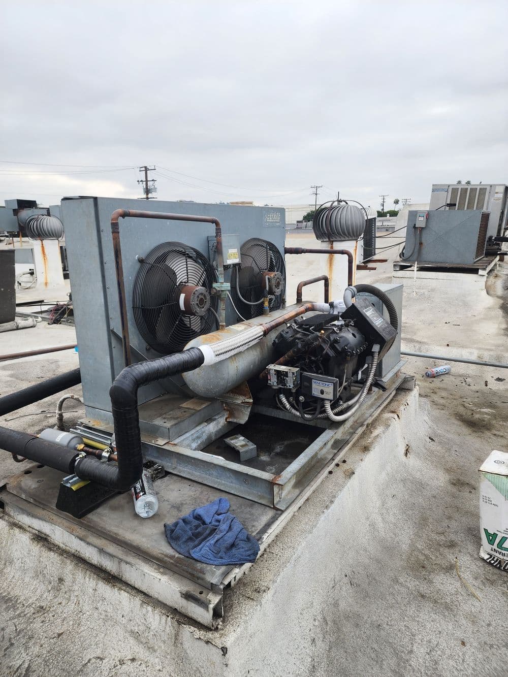 Commercial HVAC unit on rooftop with fans and piping, cloudy sky in background.