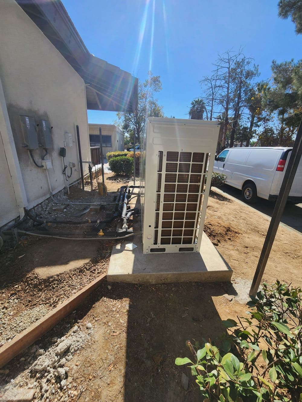 Air conditioning unit outside a building with clear blue sky and utility connections nearby.