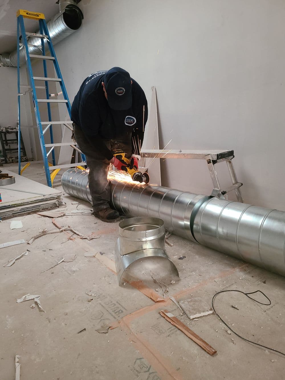 Worker cutting metal duct with a power tool in a construction space, sparks flying.