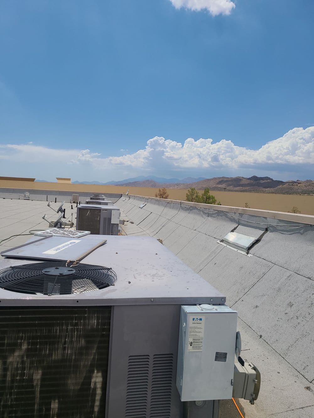 Roof-mounted HVAC units against a clear blue sky with distant mountains and clouds.